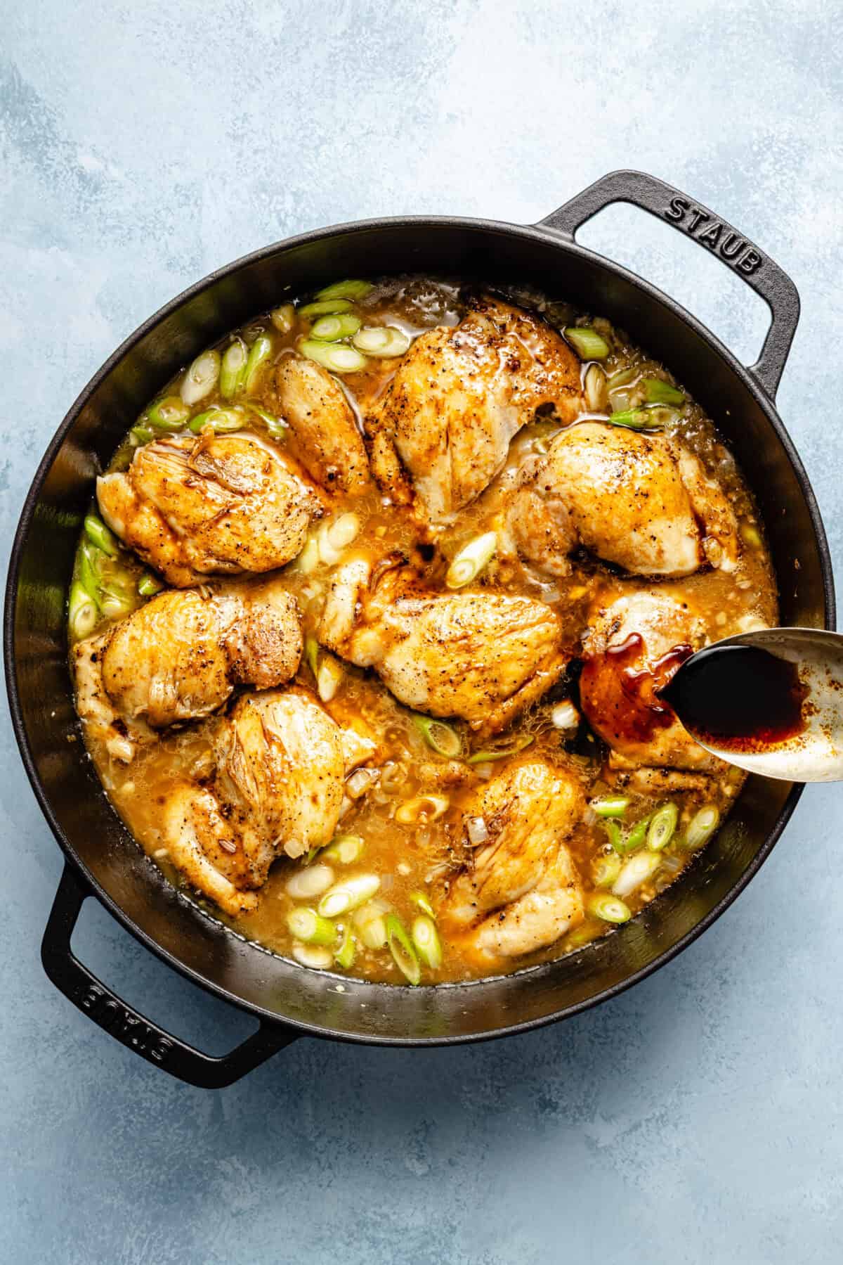 a large cast-iron skillet with chicken thighs and broth on a light blue background