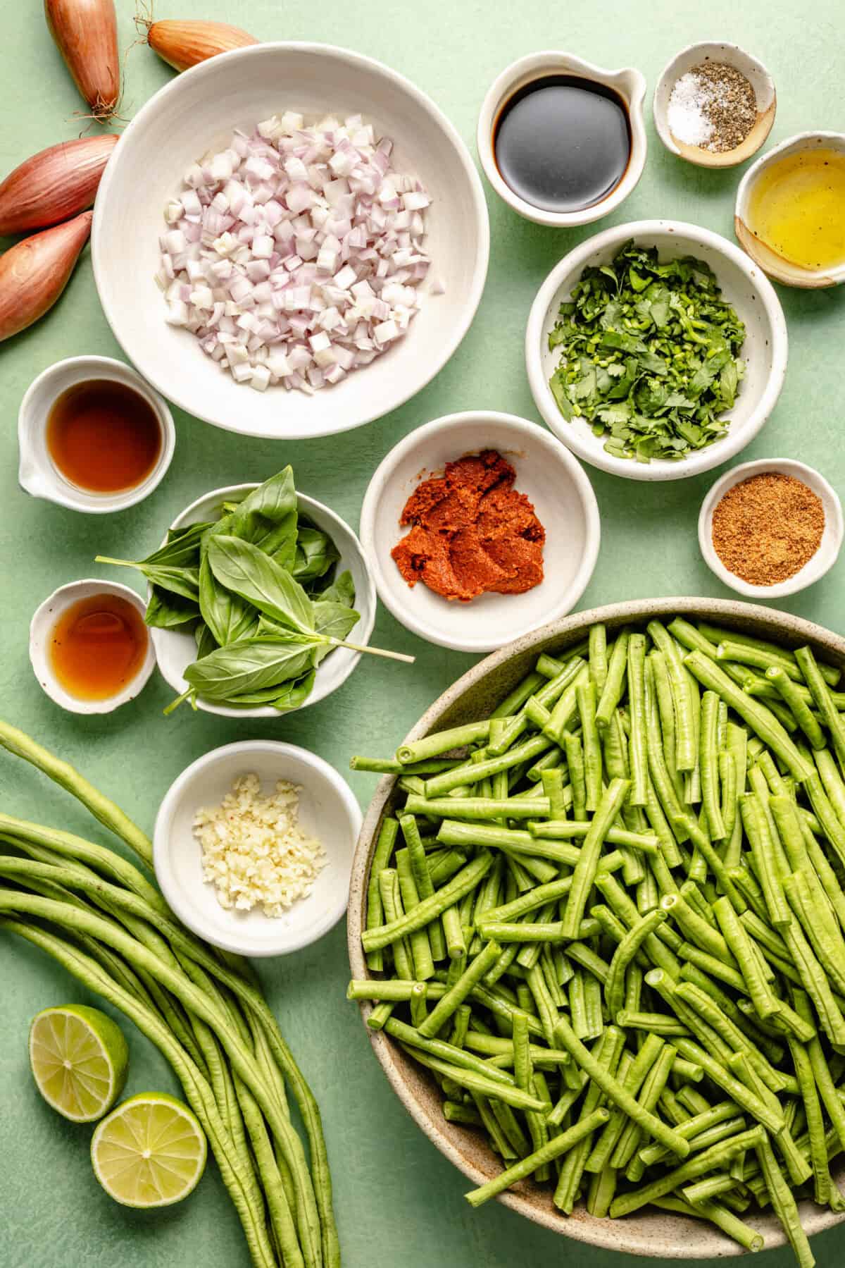 a flat-lay of ingredients for Pad Prik King including green beans, fresh herbs, and lime on a light green background