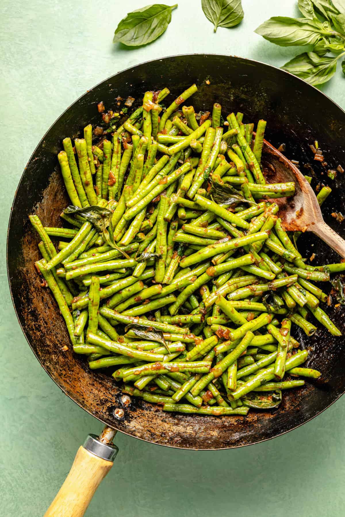 a carbon steel wok with green beans on a high green background