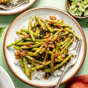 a white plate with a brown rim featuring spicy green beans over a bed of white rice