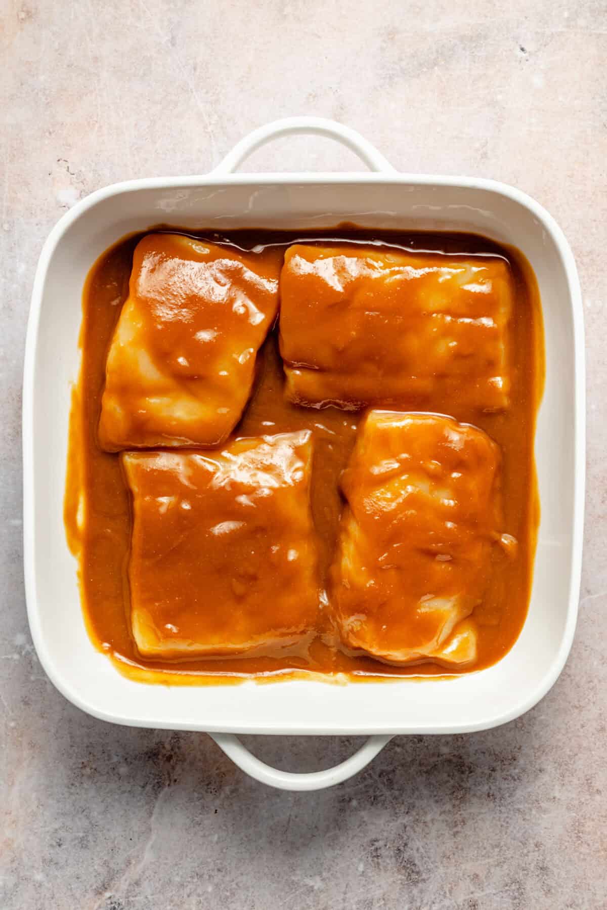 a white square baking dish with miso-marinated cod fillets on a light background