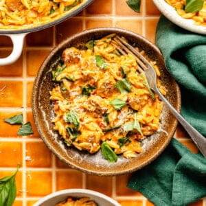 three plates of creamy tomato orzo and sausage garnished with torn fresh basil