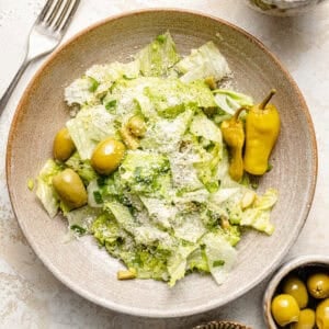 a stoneware bowl with salad greens, green olives, and pepperoncini