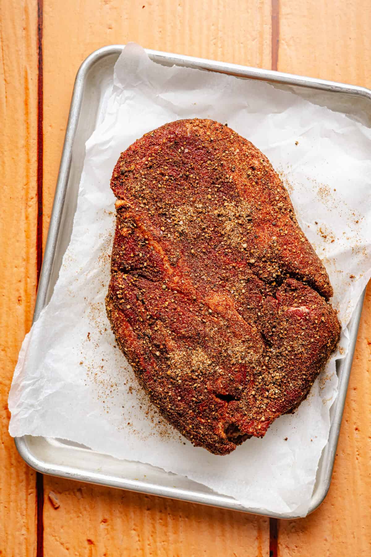 chuck roast seasoned with dried spices on a baking sheet