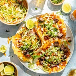 a platter of ribeye steka tacos with pickled slaw, lime wedges, onions, and cilanto