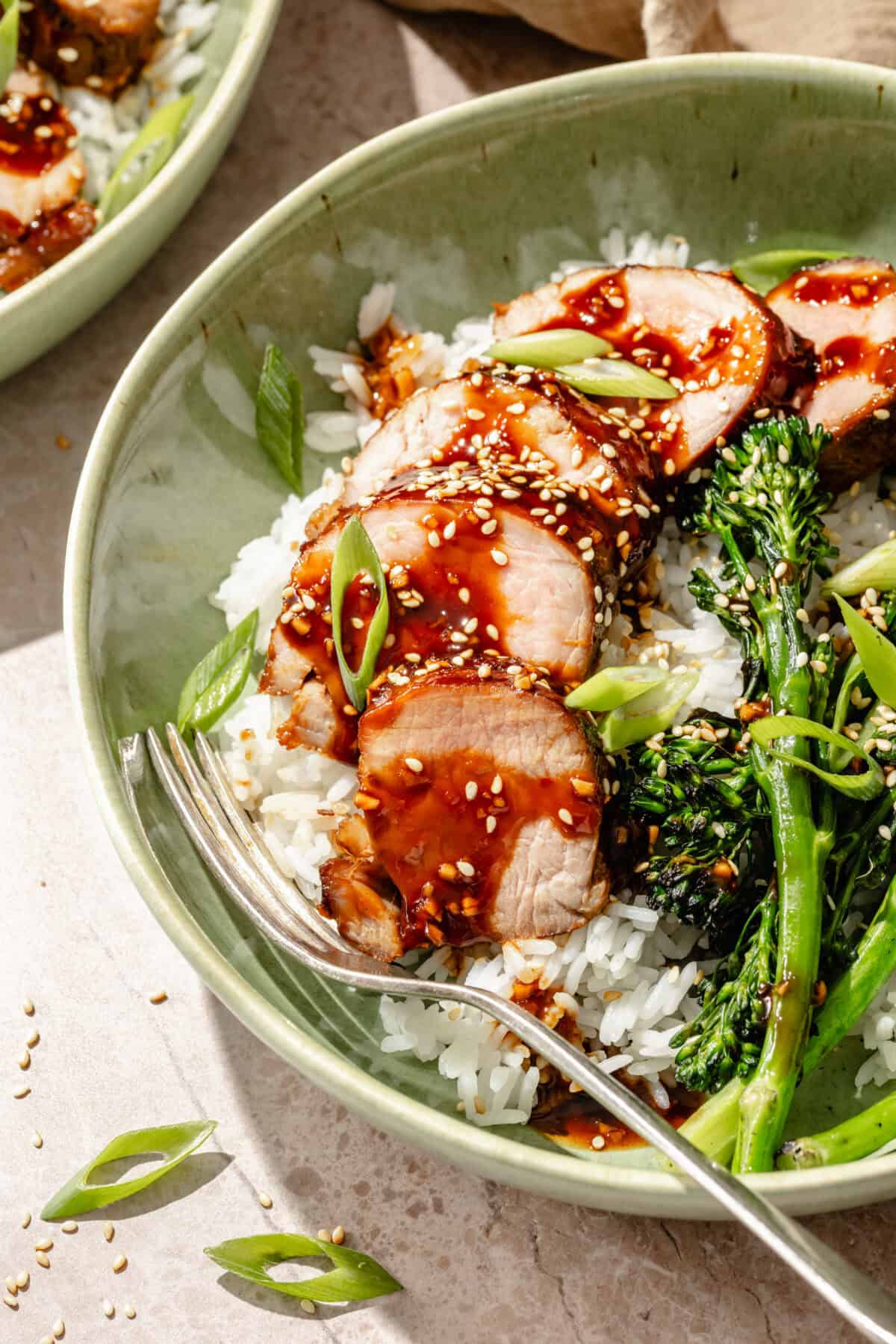 a close-up of sliced glazed hoisin pork with broccolini and white rice