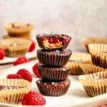 a tall stack of unwrapped and homemade almond butter and raspberry cups with chocolate