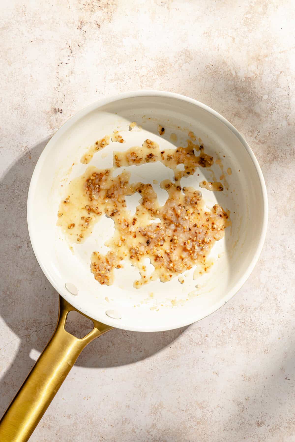 a white skillet with a gold handle on a light tan background
