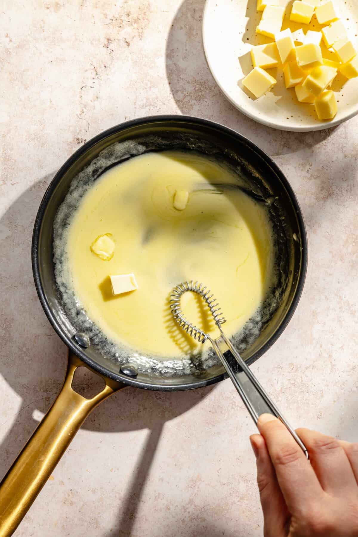 a dark skillet with melted butter and a small whisk
