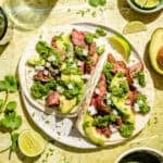 Flap Steak Tacos with Jalapeño Chimichurri assembled on plate with limes and extra sauce around.