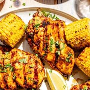 Close up of Grilled Cajun Chicken on plate with corn and lemons.