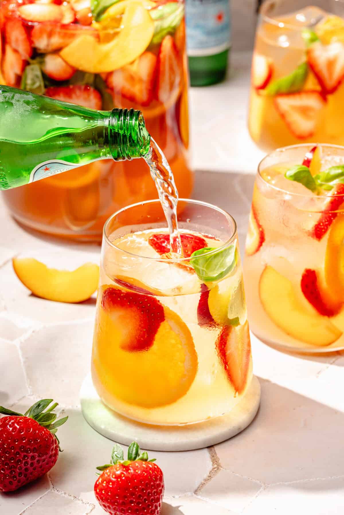 Summer Rosé Sangria in glass with sparkling water pouring in.