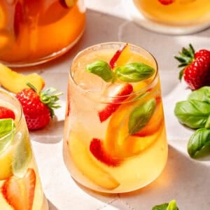 Summer Rosé Sangria in glass with a pitcher behind it.