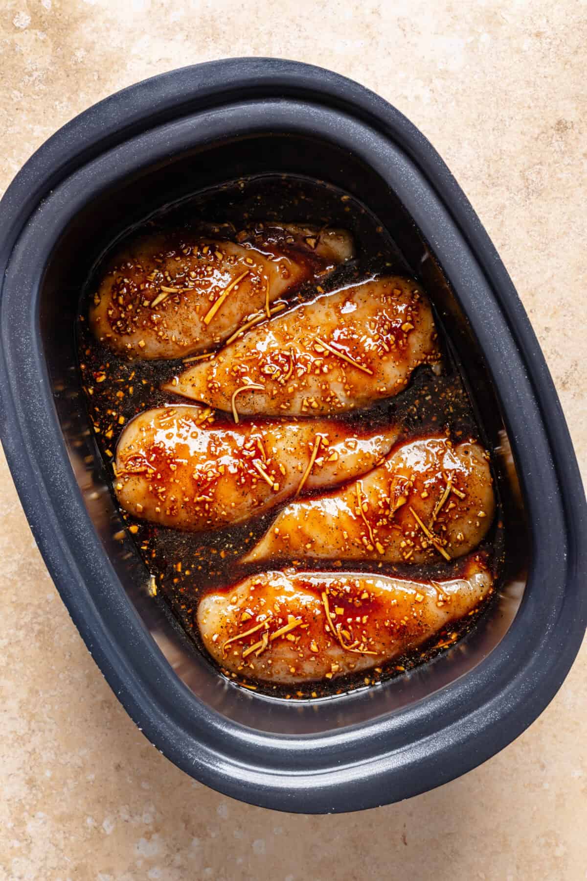 Raw chicken breasts nestled in slow cooker with sauce before it is cooked.