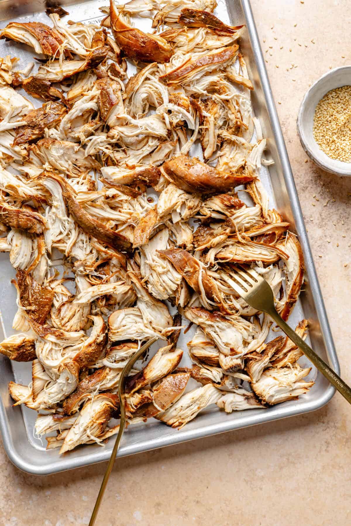 Cooked Slow Cooker Honey-Sesame Chicken shredded on sheet pan.