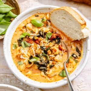 a bowl of creamy tomato soup with sausage, pasta, Parmesan cheese, and fresh basil, plus bread for dipping