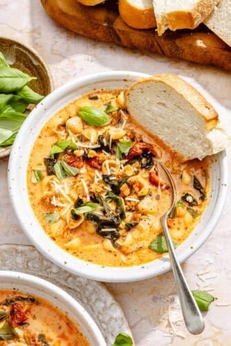 a bowl of creamy tomato soup with sausage, pasta, Parmesan cheese, and fresh basil, plus bread for dipping